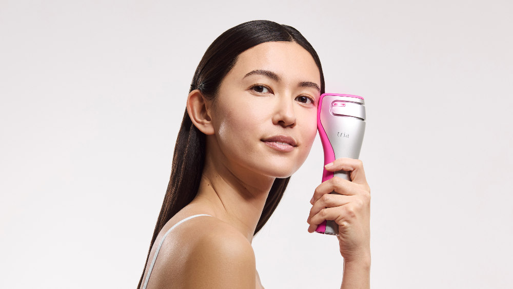 Woman holding a Tria 4X hair removal device against a white background